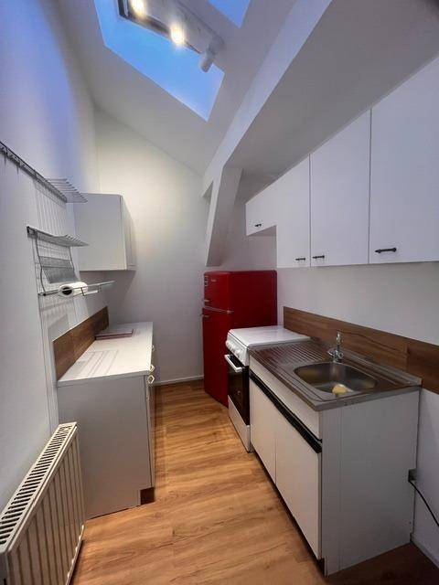 Kompakte Küche im Dachgeschoss mit rotem Kühlschrank, weißen Schränken und Dachfenster.