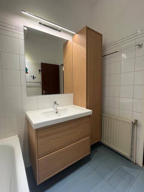 Helles Badezimmer mit Badewanne, Holzwaschtisch und großem Spiegel.