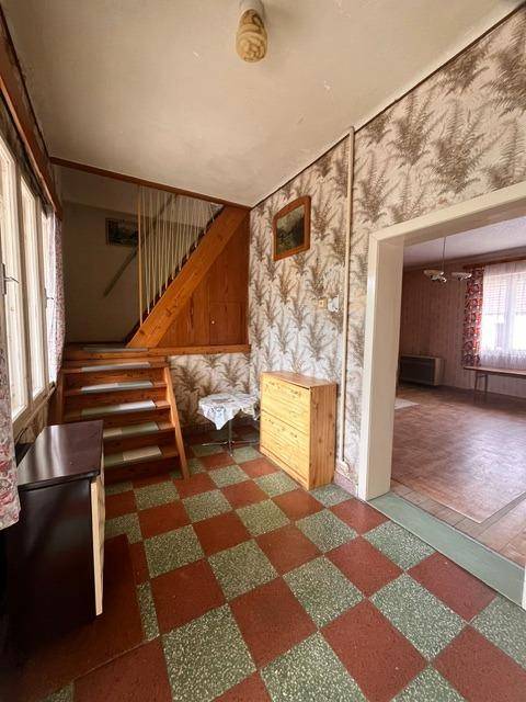 Flur mit kariertem Fliesenboden, Holztreppe und gemusterter Tapete im Vintage-Stil.