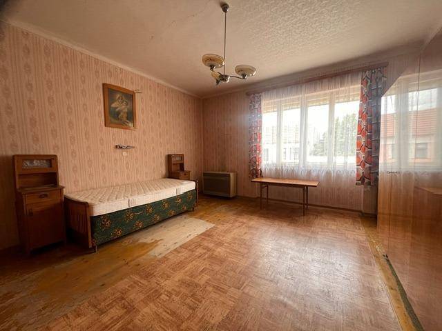 Schlafzimmer mit gemusterter Tapete, Holzfußboden und einem Fenster mit Vorhängen.