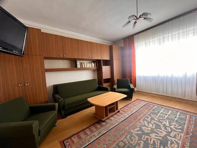Wohnzimmer mit Holzschrankwand, Teppich und einem Sofa in dunklem Grün.
