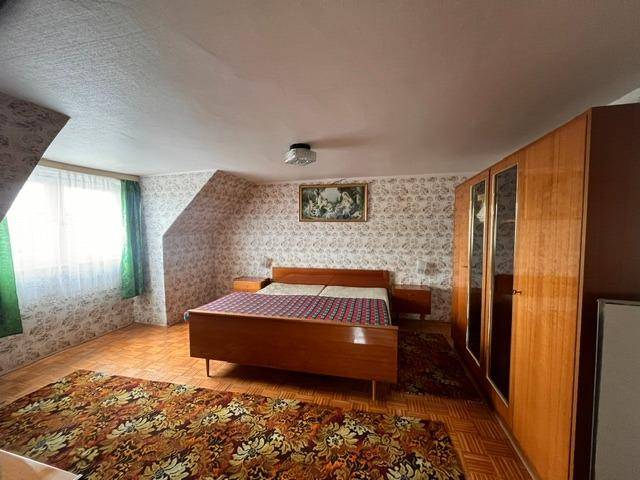 Schlafzimmer mit Doppelbett, Holzschrank und gemusterter Tapete unter Dachschrägen.