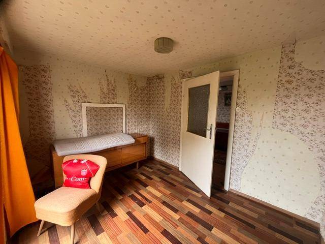 Kleines Schlafzimmer mit Holzboden, gemusterter Tapete und einem Fenster.