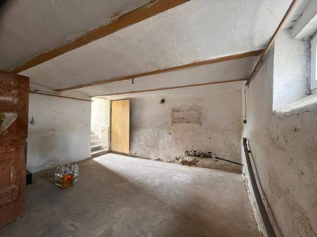 Kellerraum mit Betonboden, freiliegenden Holzbalken und einem kleinen Fenster.