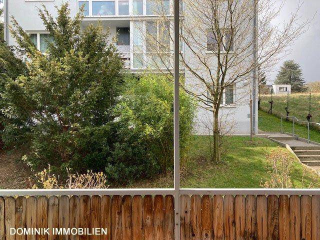 Blick vom Balkon auf die grüne Umgebung und ein angrenzendes Gebäude.