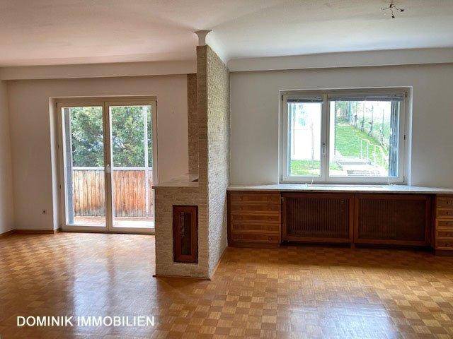 Helles Wohnzimmer mit Parkettboden, Kamin und großem Fenster mit Blick ins Grüne.