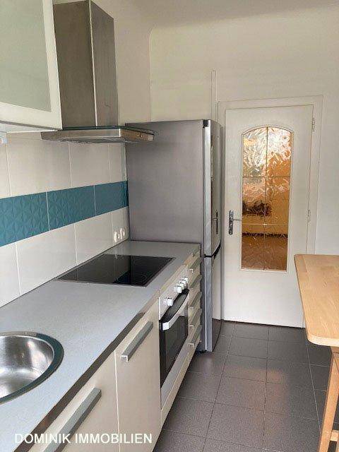 Küchenzeile mit Kühlschrank, Kochfeld und Dunstabzugshaube, daneben eine Tür.
