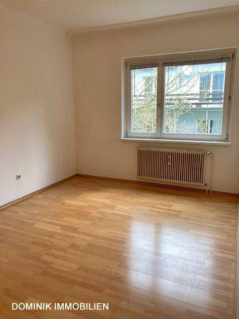 Helles Schlafzimmer mit Parkettboden und großem Fenster, bietet viel Tageslicht.
