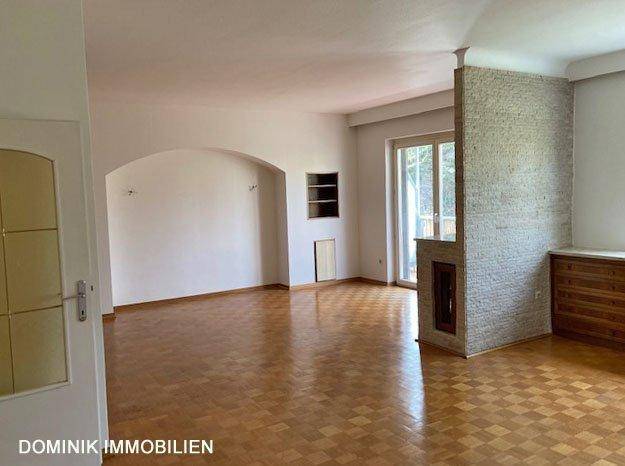 Geräumiges Wohnzimmer mit Parkettboden, einem Kamin und Zugang zum Balkon.