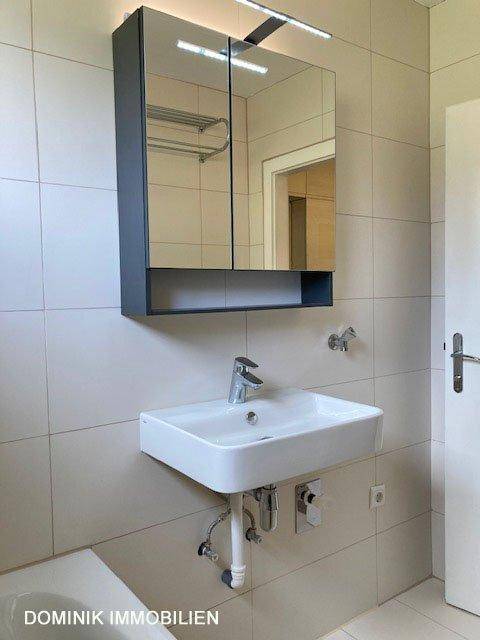 Modernes Badezimmer mit Waschbecken, Spiegelschrank und hellen Fliesen.