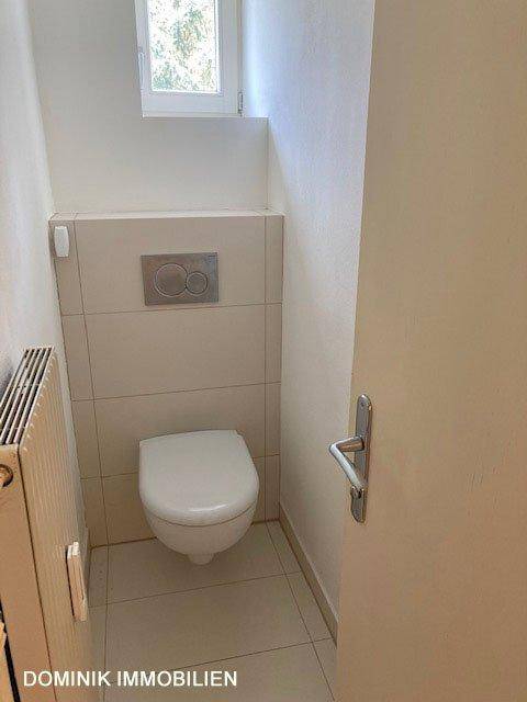 Separate Toilette mit wandhängendem WC, Heizkörper und kleinem Fenster.