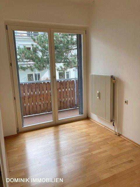 Schlafzimmer mit Parkettboden und Zugang zu einem kleinen Balkon durch eine Glastür.