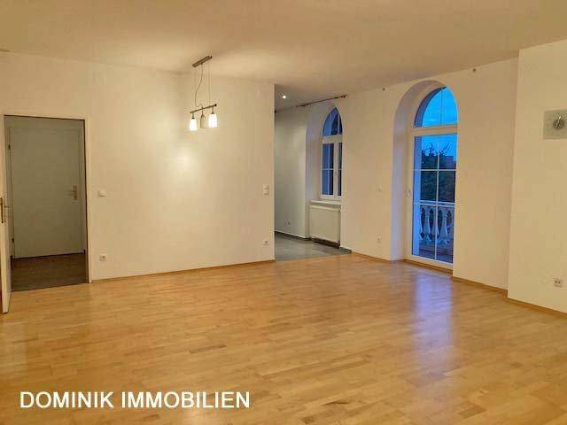 Helles, leeres Wohnzimmer mit Parkettboden und großen Rundbogenfenstern.