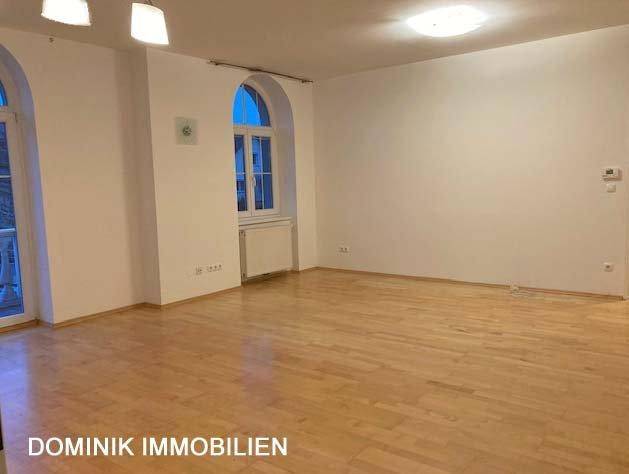 Geräumiges Wohnzimmer mit hellem Parkettboden und Blick durch Rundbogenfenster.