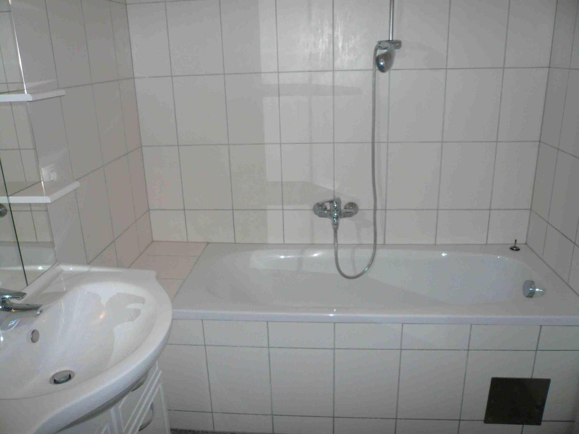 Helles Badezimmer mit Badewanne, Waschbecken und weißen Wandfliesen.