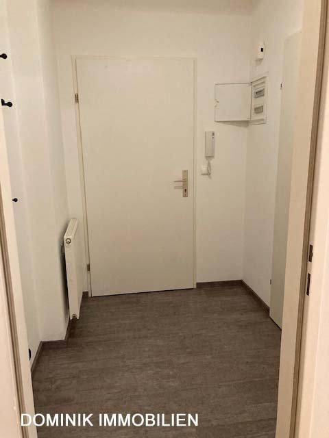 Eingangsbereich mit dunklem Boden, weißer Tür und Gegensprechanlage.