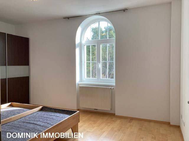 Schlafzimmer mit Parkettboden und einem hohen Rundbogenfenster, das viel Licht spendet.