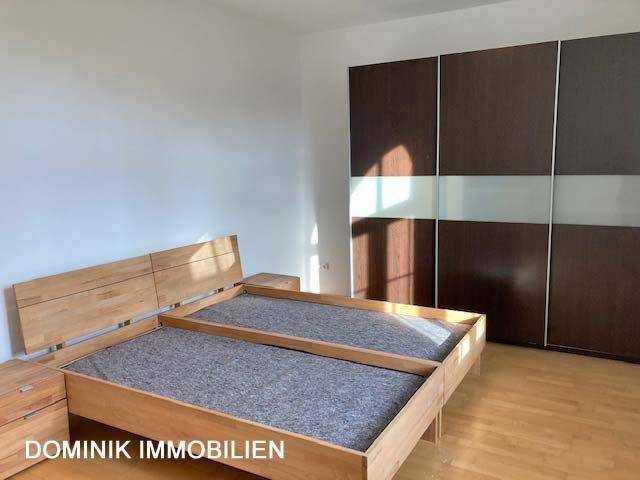 Schlafzimmer mit Holzbettrahmen und großem Schiebetürenschrank in dunkler Holzoptik.