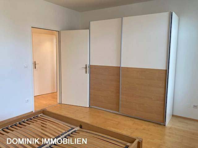 Schlafzimmer mit Parkettboden und einem modernen Schiebetürenschrank in Holzoptik.