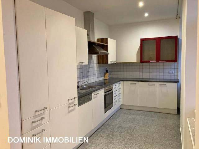 Moderne Einbauküche mit weißen Schränken, dunkler Arbeitsplatte und Fliesenboden.