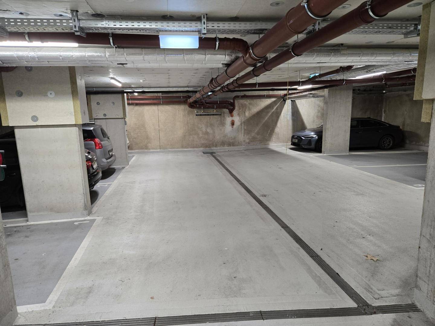 Geräumige Tiefgarage mit mehreren Stellplätzen, Betonwänden und sichtbaren Versorgungsleitungen.