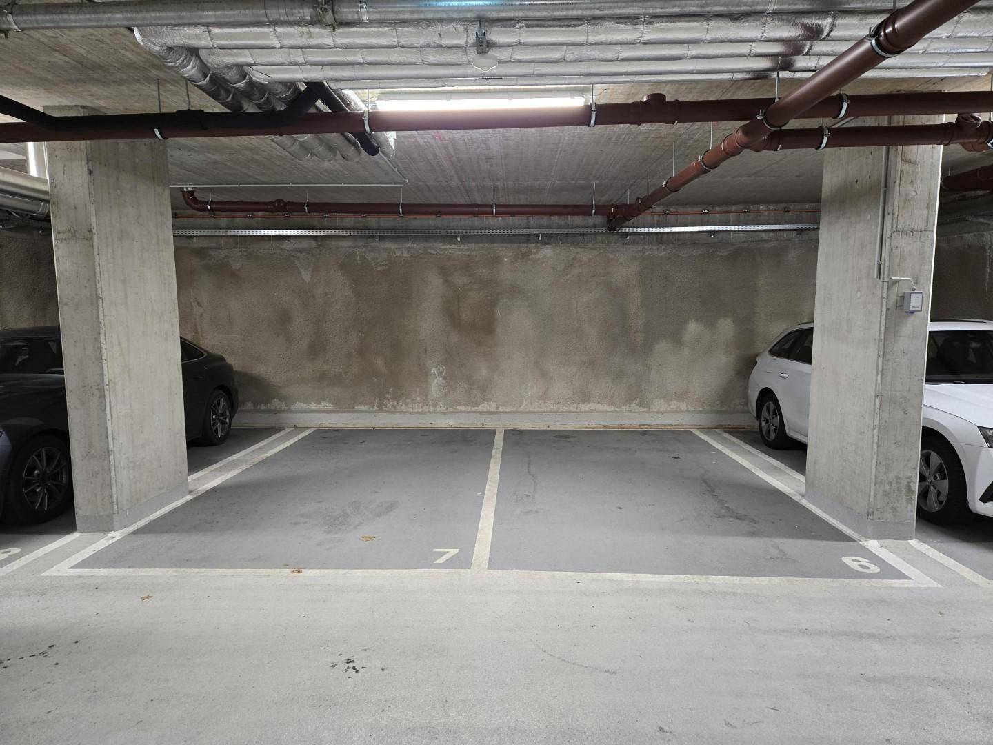 Zwei markierte Stellplätze in einer Tiefgarage mit Betonwänden und sichtbaren Rohrleitungen an der Decke.