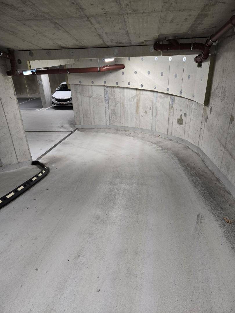 Gebogene Rampe in einer Tiefgarage mit Betonwänden und sichtbaren Installationen.