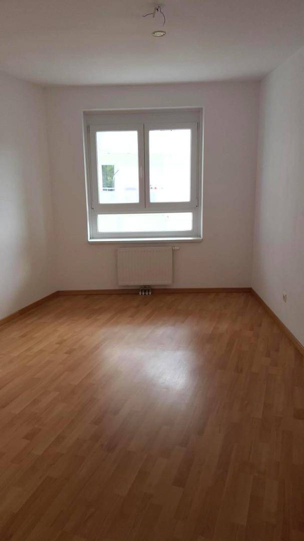 Helles Schlafzimmer mit Parkettboden, großem Fenster und Heizkörper unter dem Fenster.