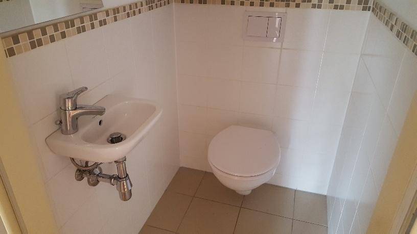 Gäste-WC mit wandhängender Toilette, kleinem Waschbecken und gefliesten Wänden.