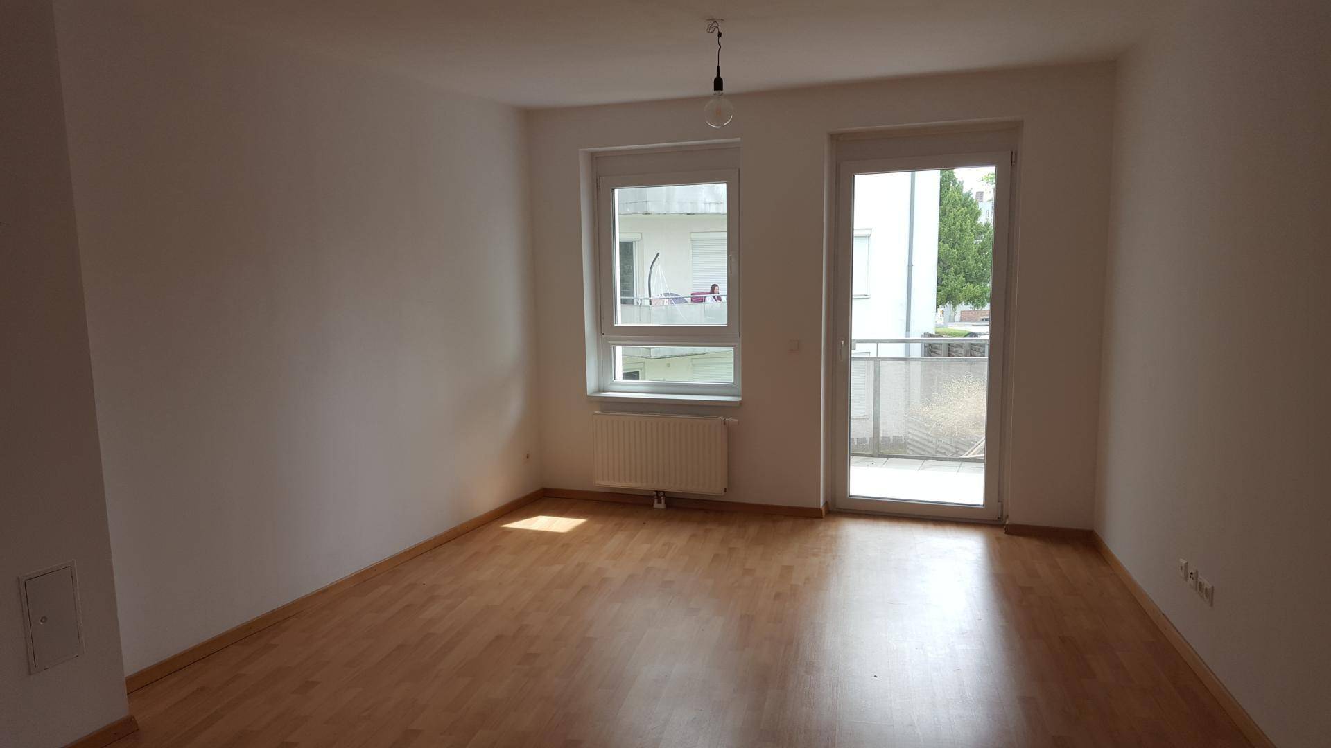 Heller Raum mit Parkettboden, großem Fenster und Zugang zu einem kleinen Balkon.