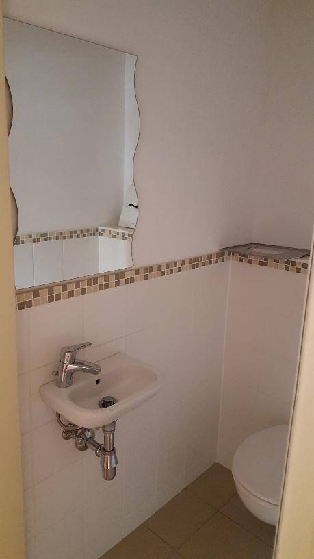Gäste-WC mit Waschbecken, Spiegel und wandhängender Toilette, gefliesten Wänden.