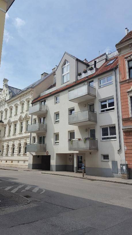 Fassade eines Mehrfamilienhauses mit Balkonen und angrenzenden Altbauten an einer Straße.