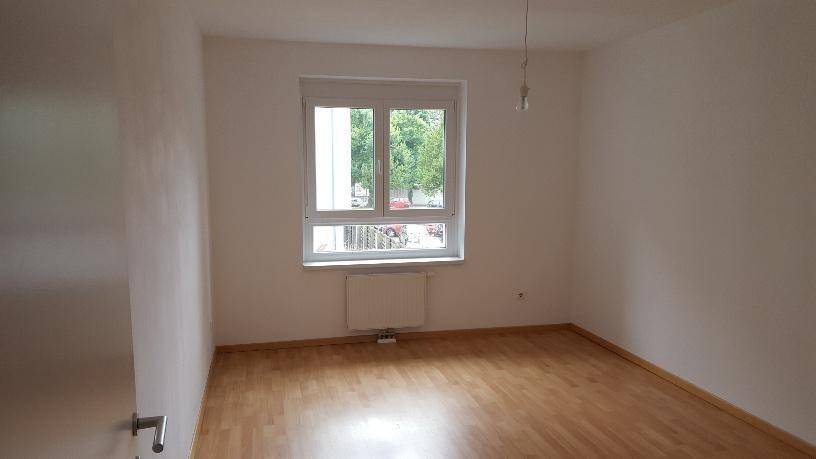 Lichtdurchflutetes Zimmer mit Parkettboden und Blick ins Grüne durch das Fenster.