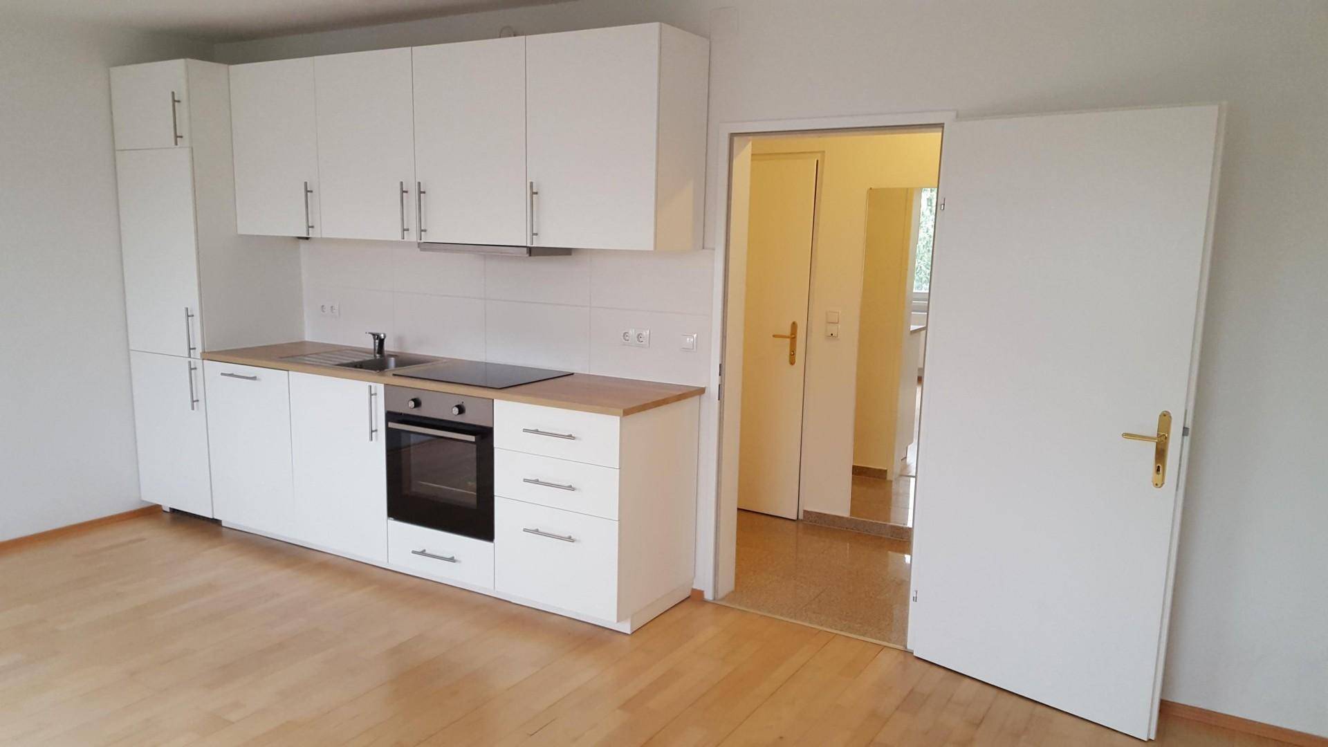 Moderne Einbauküche mit weißen Schränken, Holzarbeitsplatte und Parkettboden.