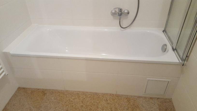 Badezimmer mit eingebauter Badewanne, Duscharmatur und Fliesen an den Wänden.