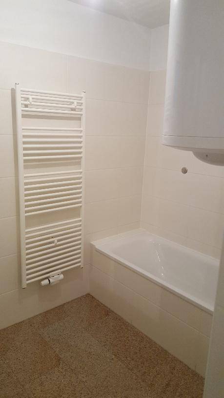 Badezimmer mit Badewanne, beheiztem Handtuchhalter und einem Warmwasserboiler.