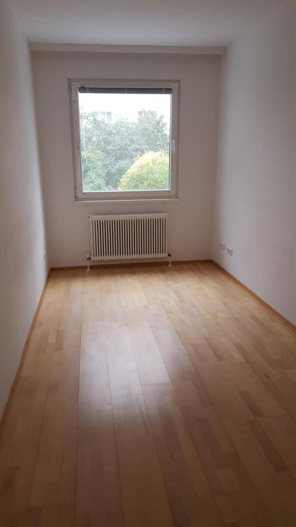 Helles Zimmer mit Parkettboden, einem großen Fenster und Blick ins Grüne.