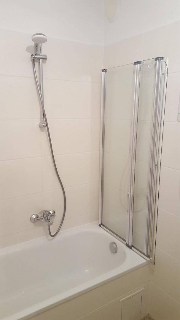 Badewanne mit Duscharmatur und einer faltbaren Duschwand aus Glas.