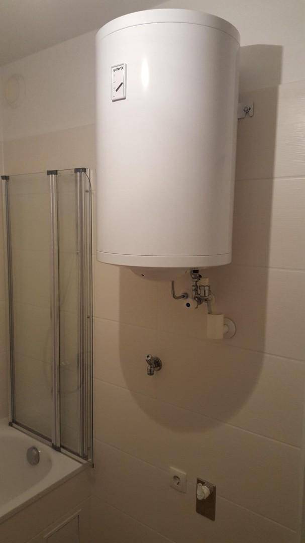 Wandmontierter Warmwasserboiler über der Badewanne mit Duschwand.