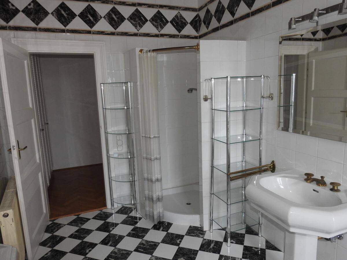 Geräumiges Badezimmer mit Duschkabine, Standwaschbecken und markantem schwarz-weißem Fliesenmuster.