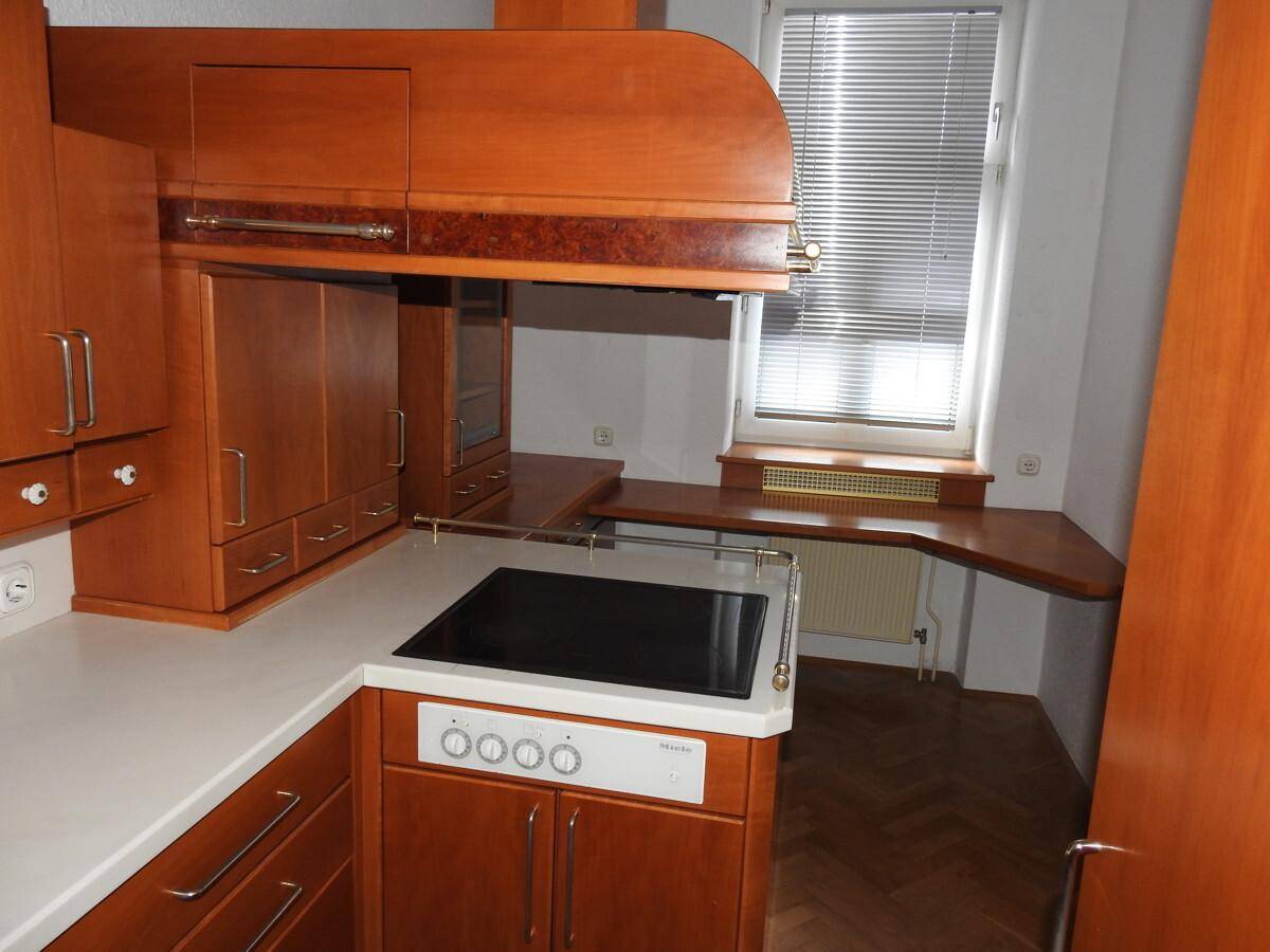 Funktionale Küche mit Holzeinbauschränken, integriertem Kochfeld und Arbeitsfläche unter dem Fenster.