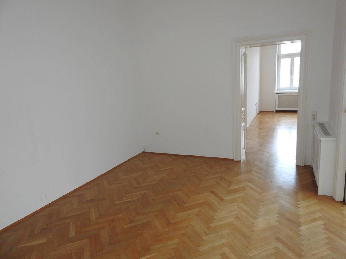 Leeres Zimmer mit klassischem Fischgrätparkett und weiß gestrichenen Wänden, bereit zur Einrichtung.