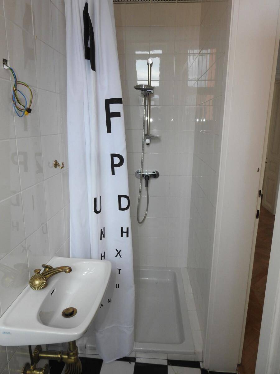 Kleines Badezimmer mit Duschkabine, Waschbecken und markantem schwarz-weiß kariertem Fliesenboden.