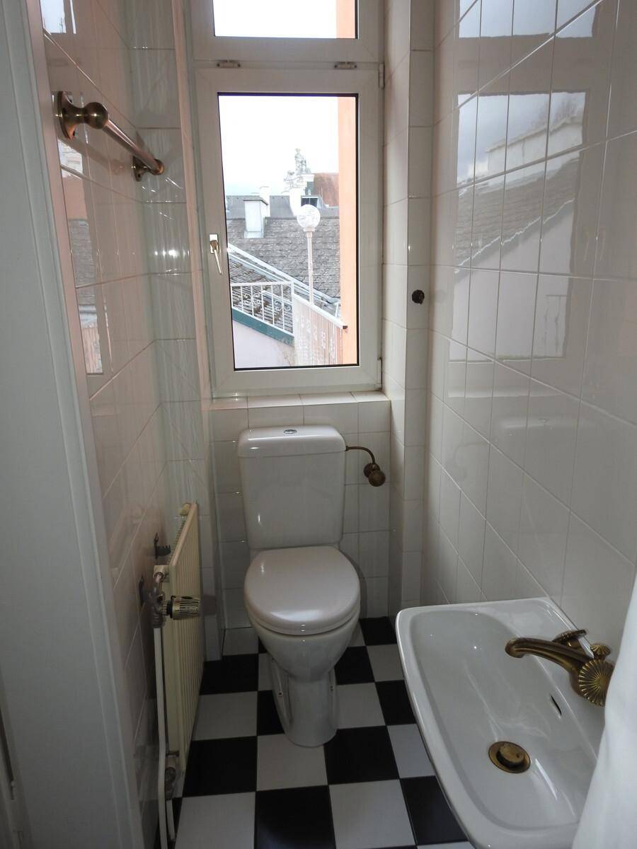 Helles WC mit Fenster, Toilette, Waschbecken und auffälligem schwarz-weißem Fliesenbodenmuster.
