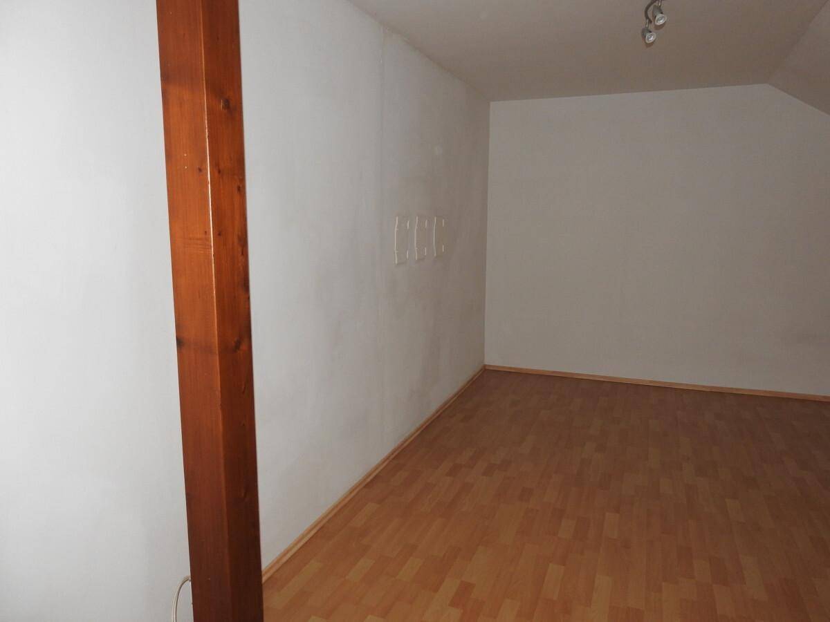 Leerer Raum mit Holzbalken, Dachschräge und Laminatboden, bereit zur individuellen Gestaltung.