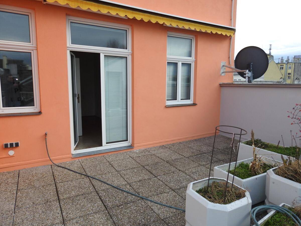 Zugang zur Terrasse mit orangefarbener Fassade, Fenstern und einer gelben Markise über dem Eingang.