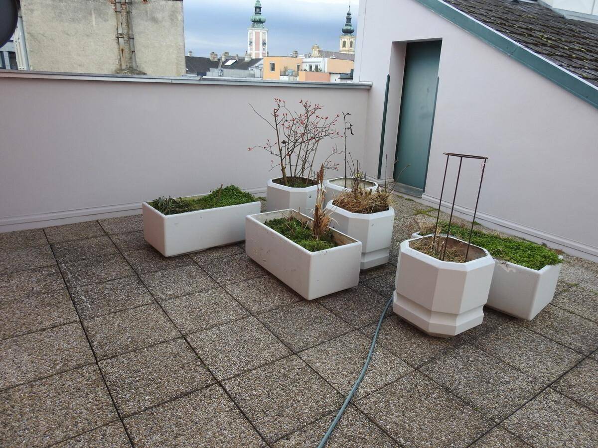 Gedeckte Terrasse mit Pflanzkübeln und Fliesenboden, bereit für individuelle Gestaltung und Bepflanzung.