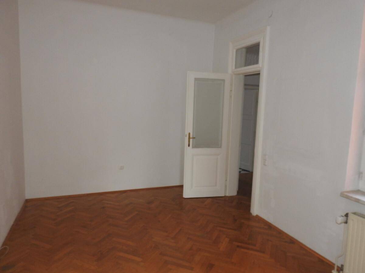 Ruhiges Zimmer mit Fischgrätparkett und einer Tür, die zu einem weiteren Raum führt.