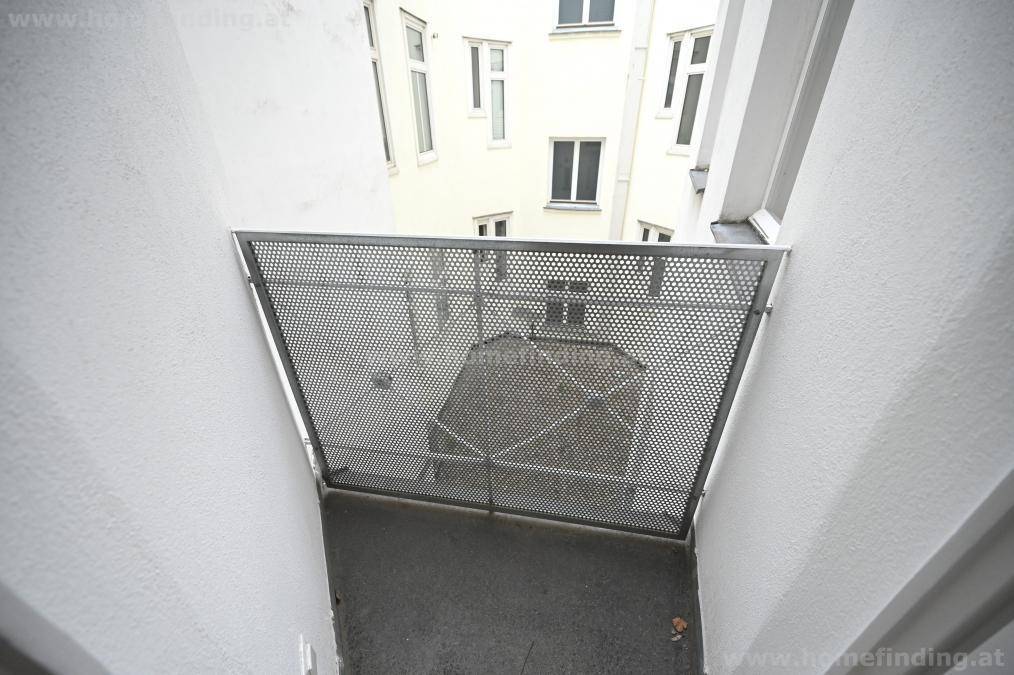 Kleiner Balkon mit Metallgitter und Blick auf den Innenhof des Gebäudes.