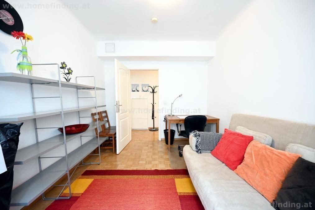 Helles Arbeitszimmer mit Regalen, Sofa und Zugang zu einem weiteren Bereich der Wohnung.